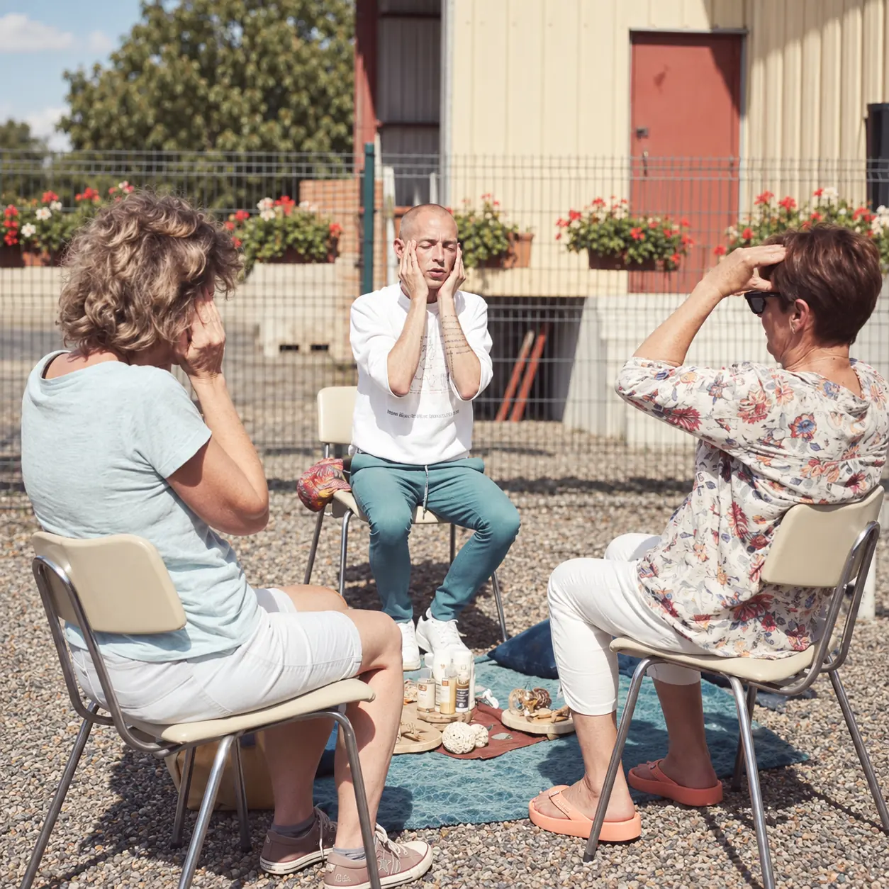 Trois personnes assises en extérieur, les mains posées sur leur propre visage lors d’une démonstration.