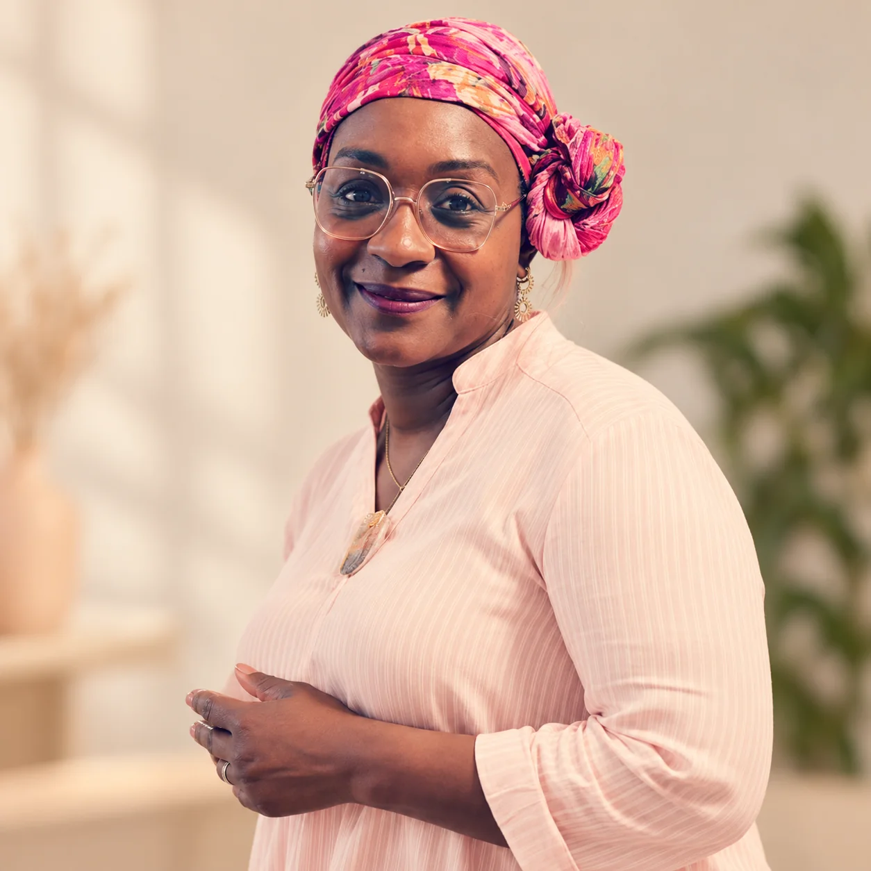 Portrait d’une femme souriante portant un turban coloré et une tenue claire.