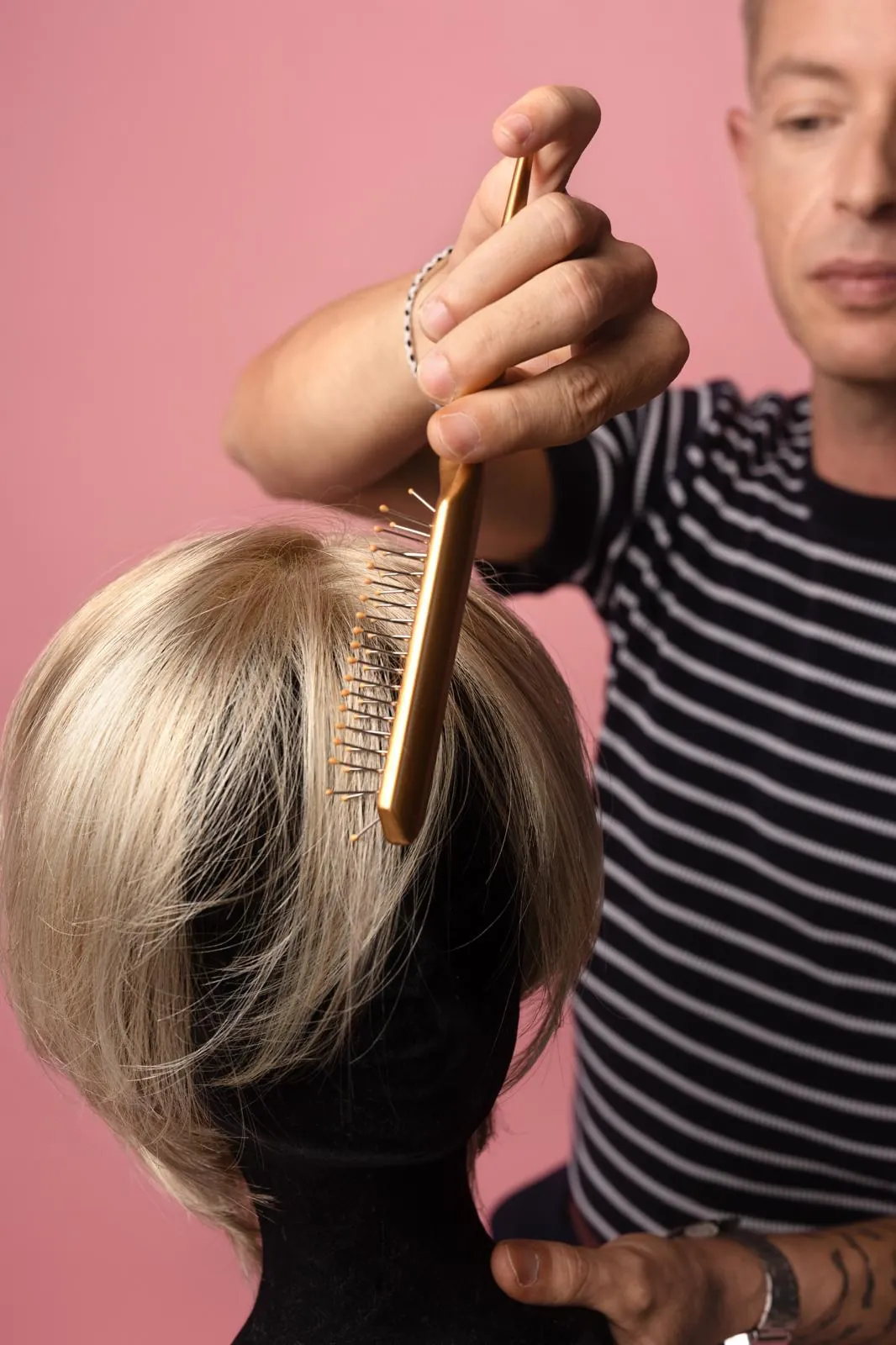 Benjamin Froidure coiffe une perruque blonde sur une tête de présentation, sur fond rose.