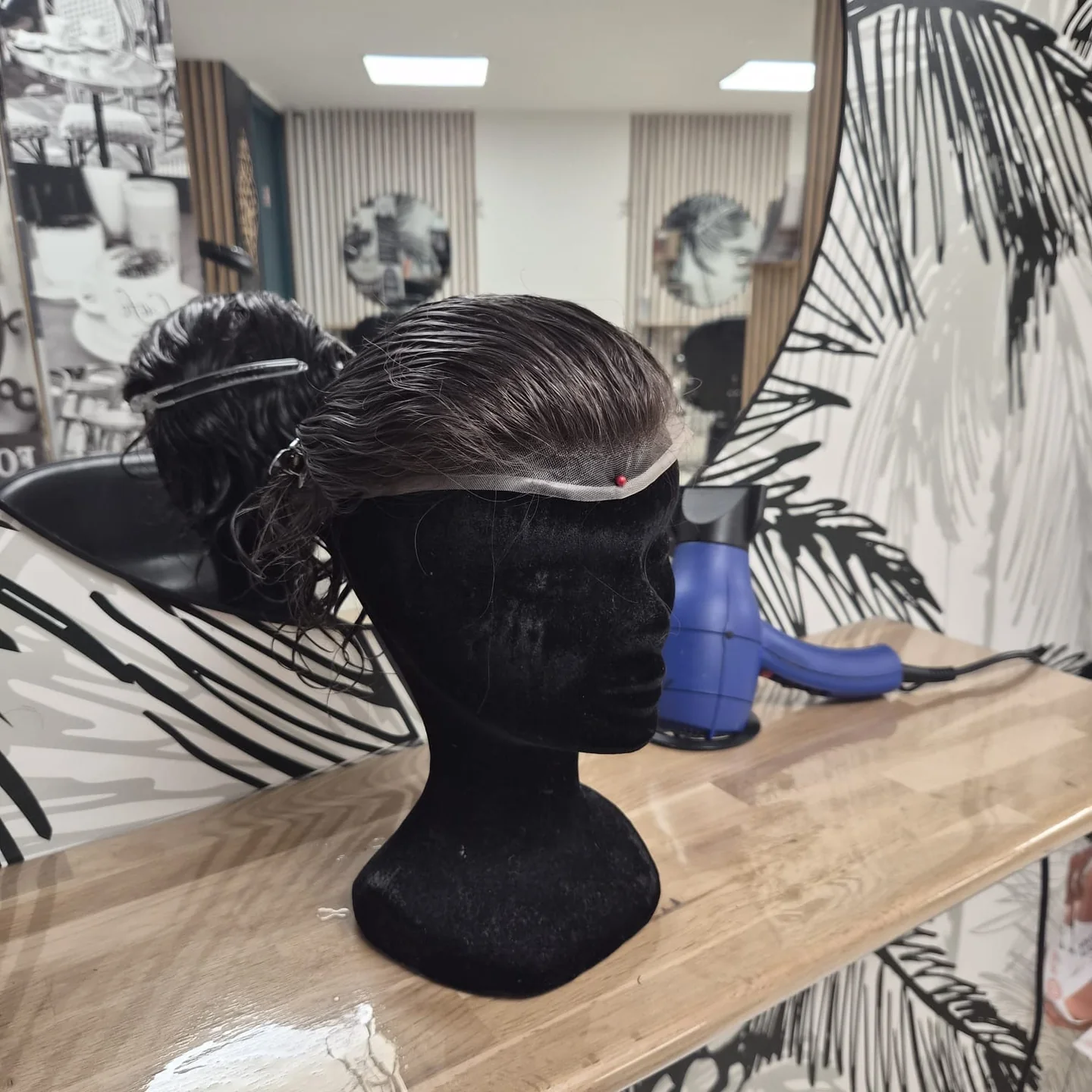 Chevelure courte brune présentée sur un support noir devant un miroir.
