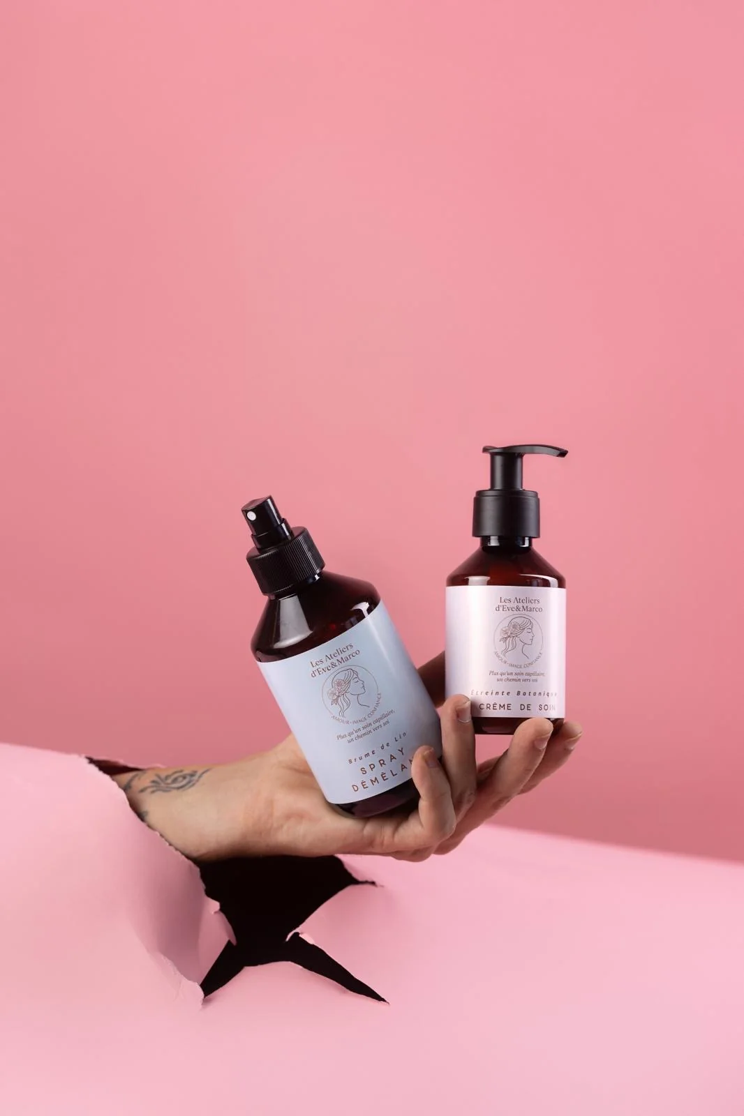 Deux flacons Les Essences Yiel tenus dans une main sur fond rose.