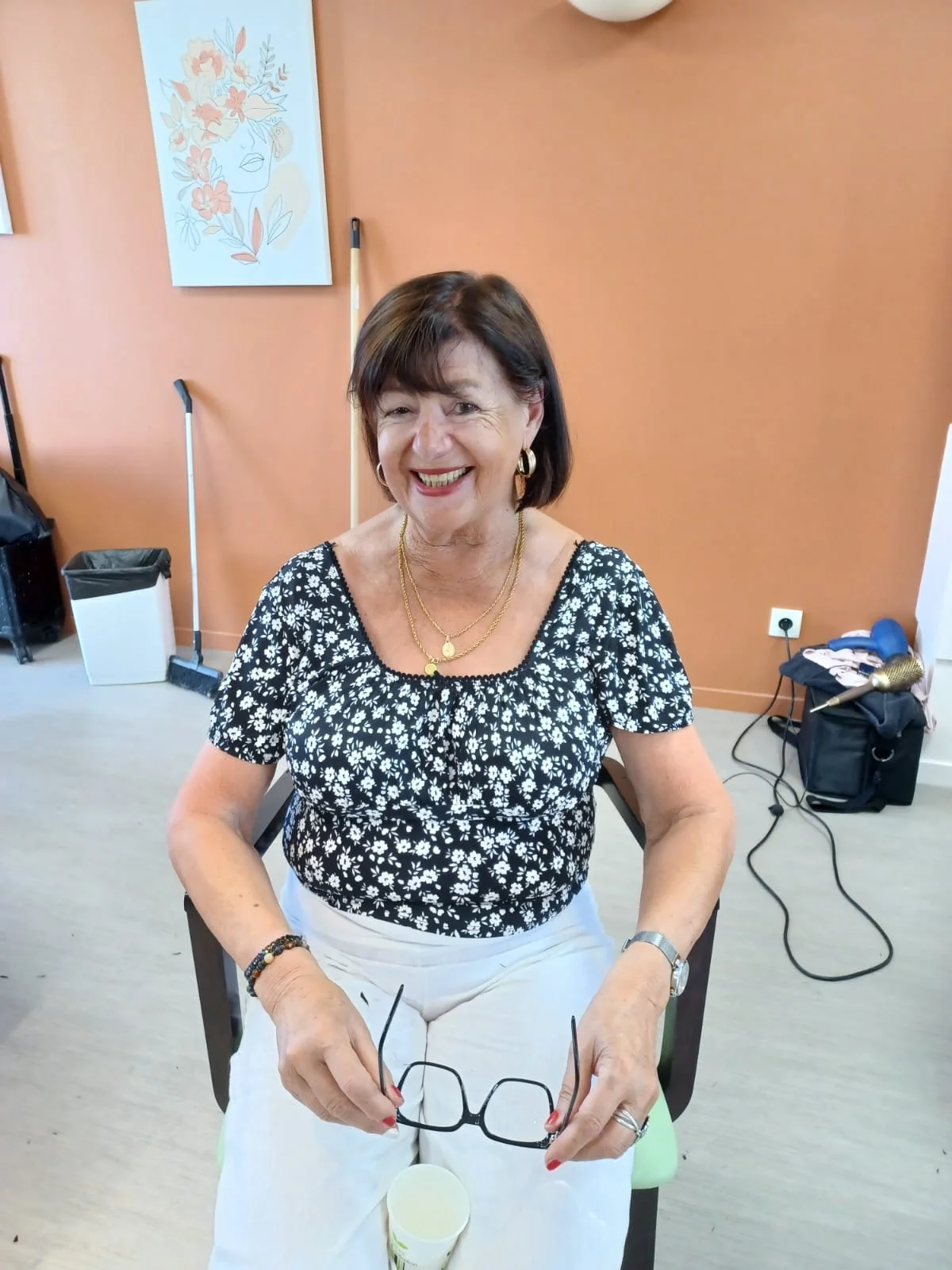 Une femme souriante aux cheveux courts bruns, vêtue d’un haut fleuri.