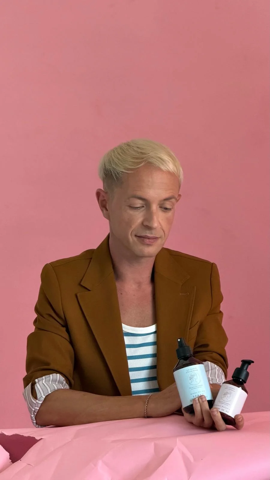 Benjamin Froidure en veste brune présente des soins Les Essences Yiel sur fond rose.